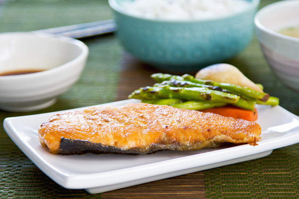 Sepotong salmon panggang berwarna keemasan, disajikan dengan perasan lemon