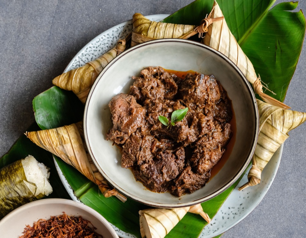 Rendang daging sapi dalam piring dikelilingi ketupat.