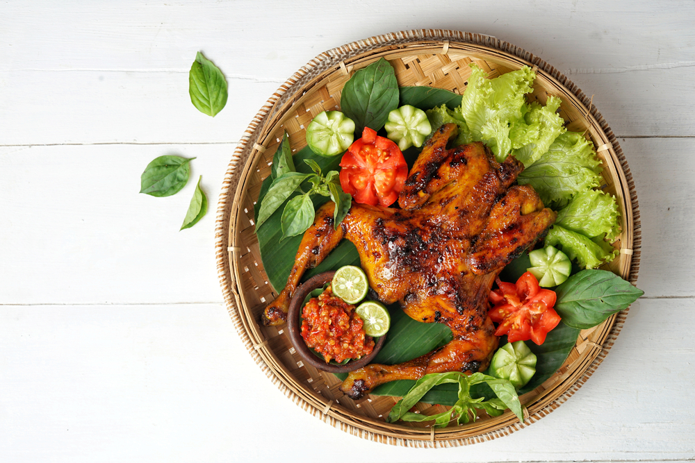 Ayam bakar ungkep beserta lalapan sayuran dalam wadah bambu.