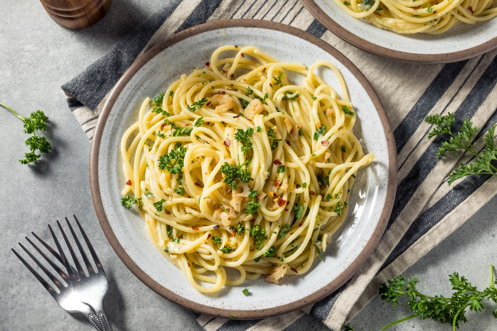 Spaghetti aglio olio dalam piring saji putih dengan alas serbet.