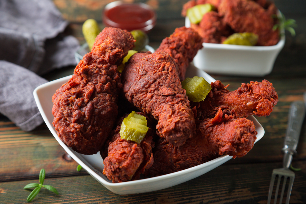 Nashville hot chicken dalam piring saji putih dengan acar gerkins.