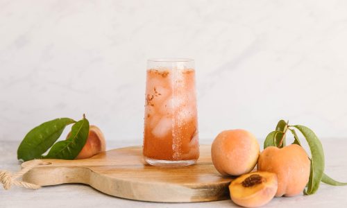 Segelas peach tea di atas talenan dengan buah peach segar di sisinya.